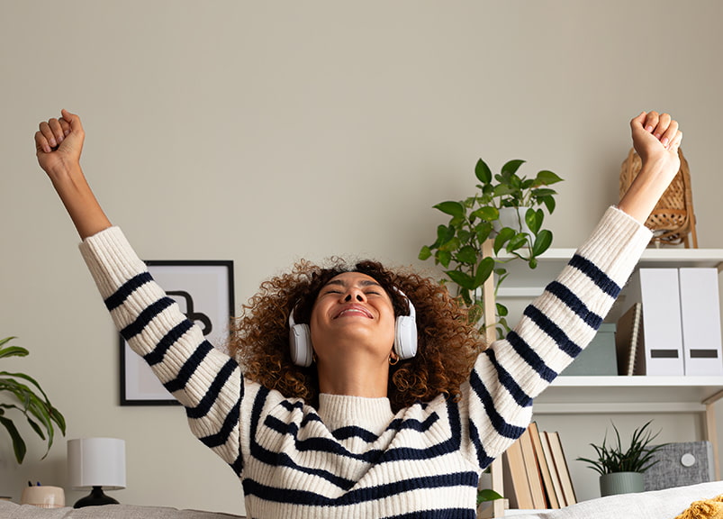 Woman sitting on a couch with a laptop and headset, joyfully raising her hands